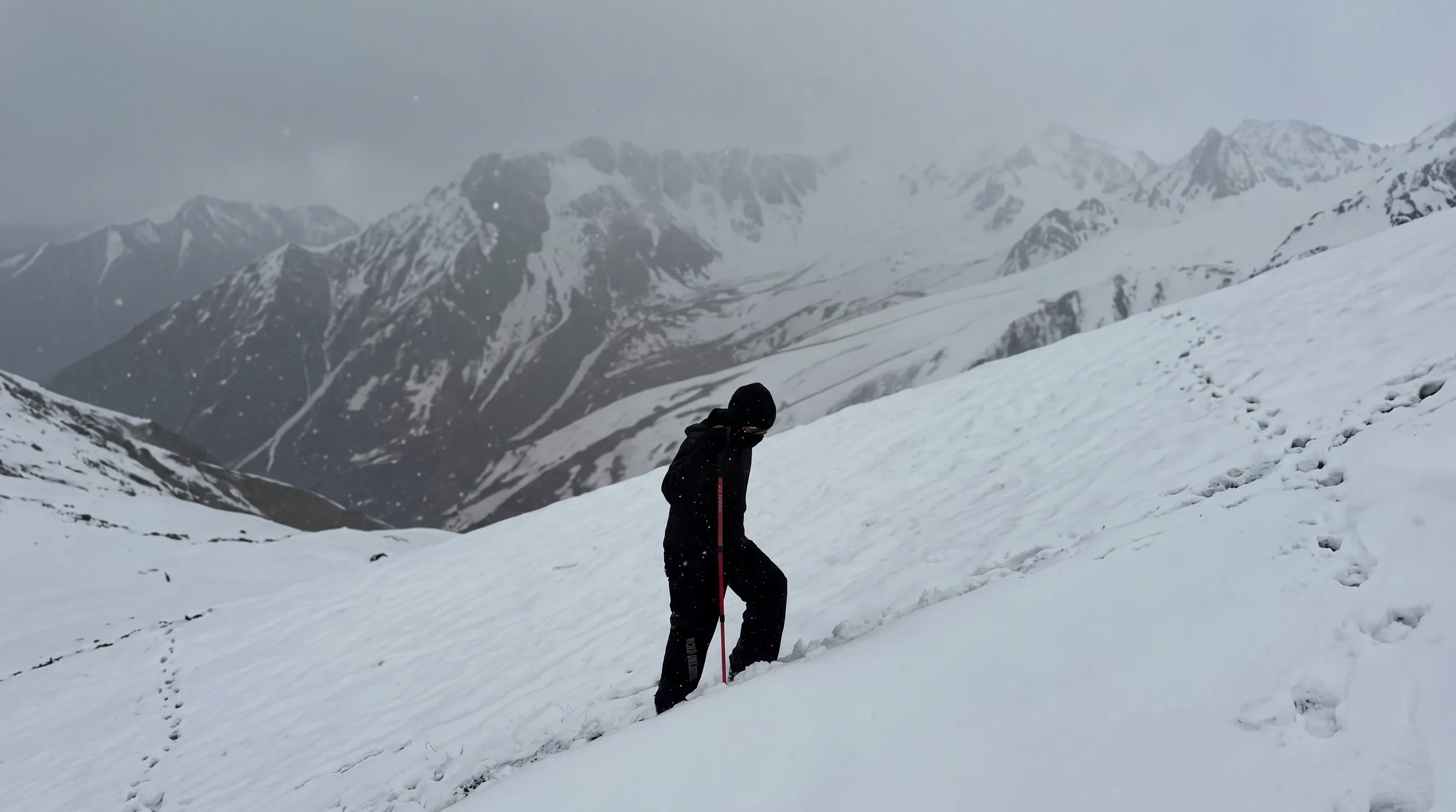 Solo trekker ascending steep snow slope in blizzard