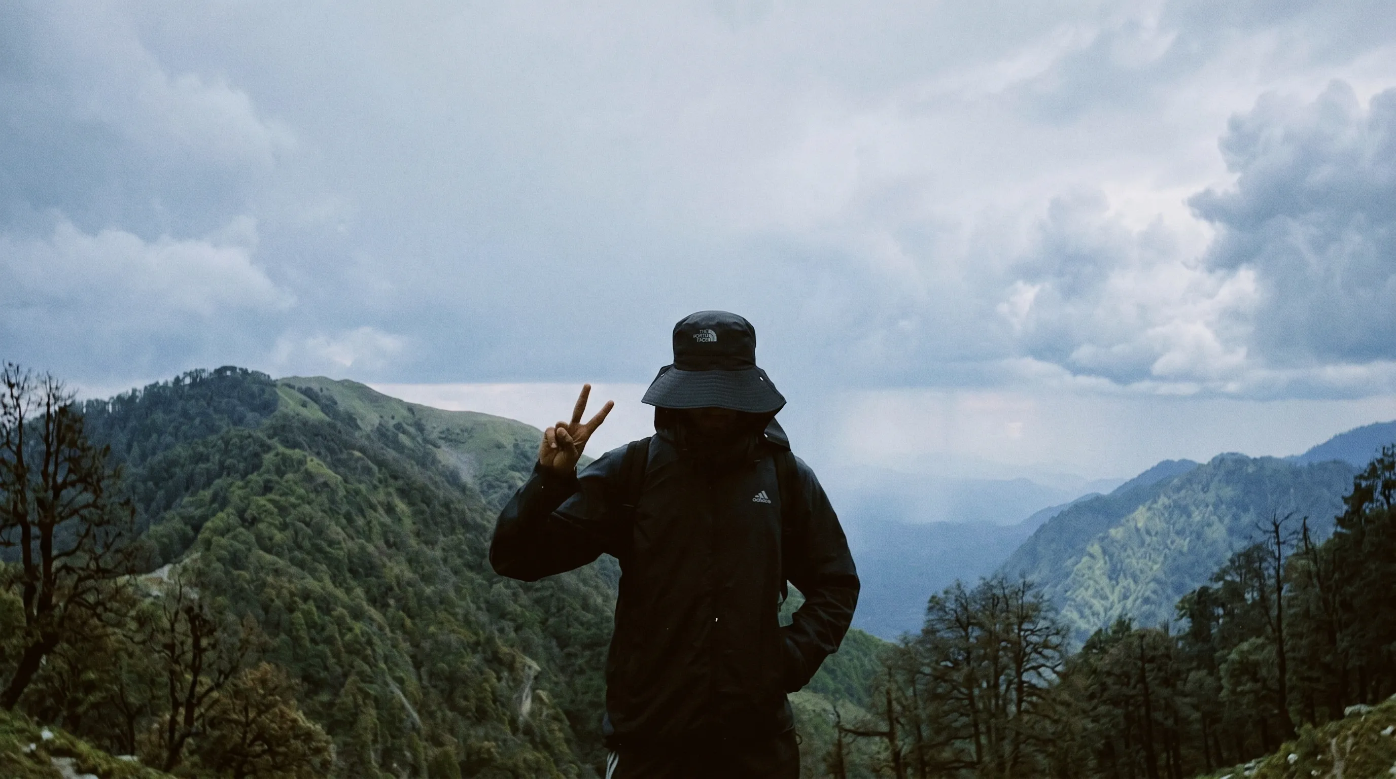Trekker with peace sign overlooking mountain forest valley