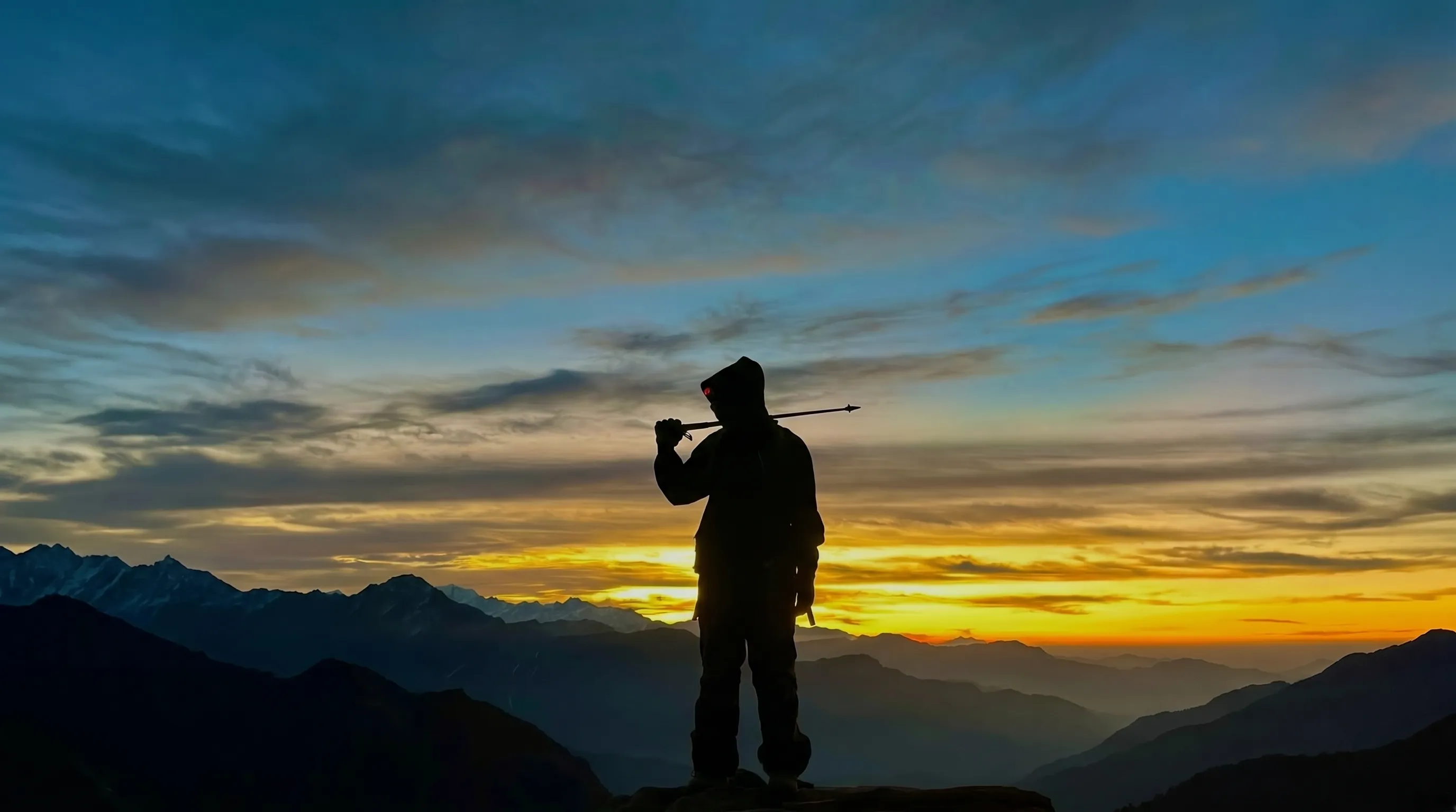 Silhouette against Himalayan golden sunset, trekking pole raised